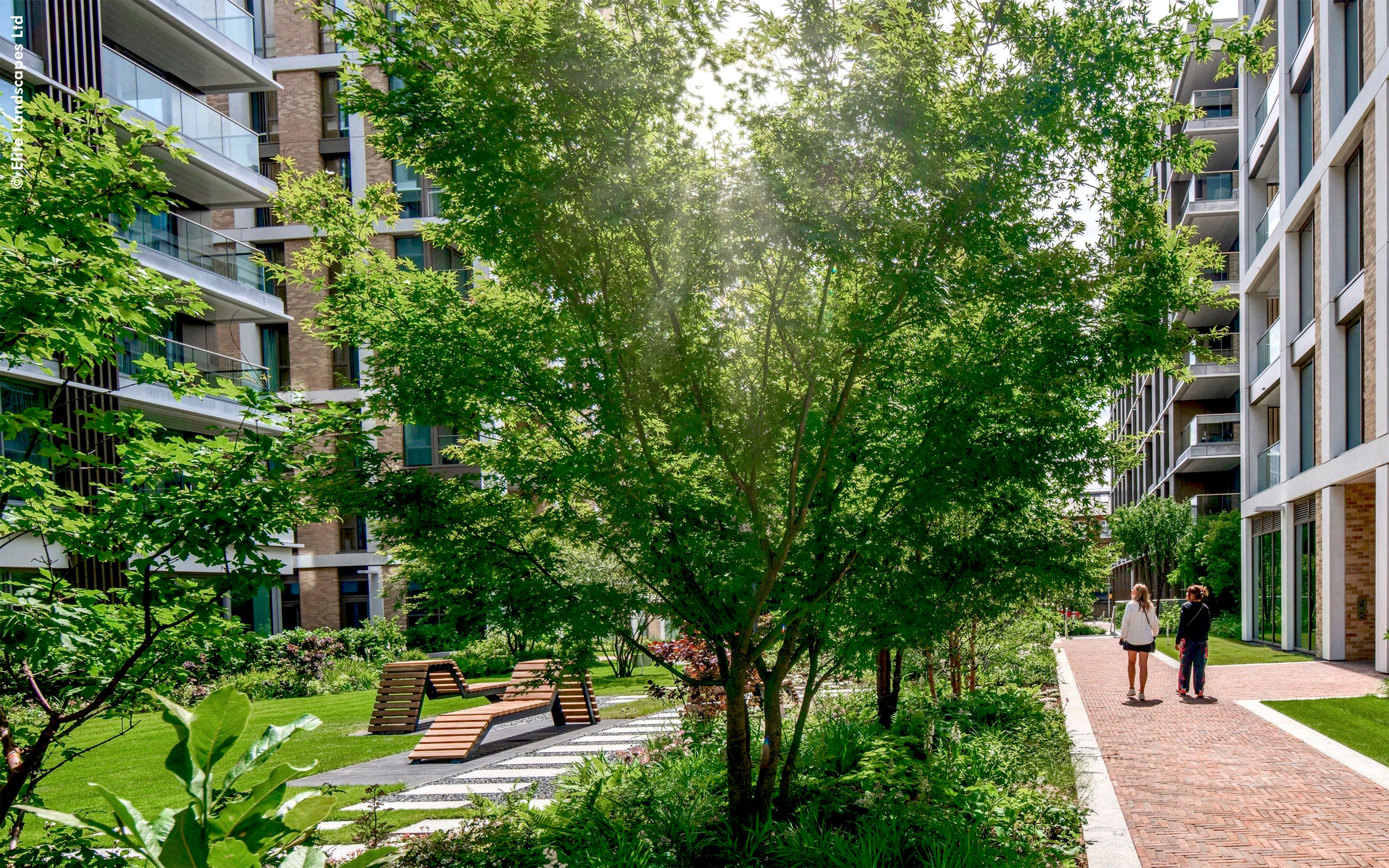 People stroll through a green courtyard of a residential complex