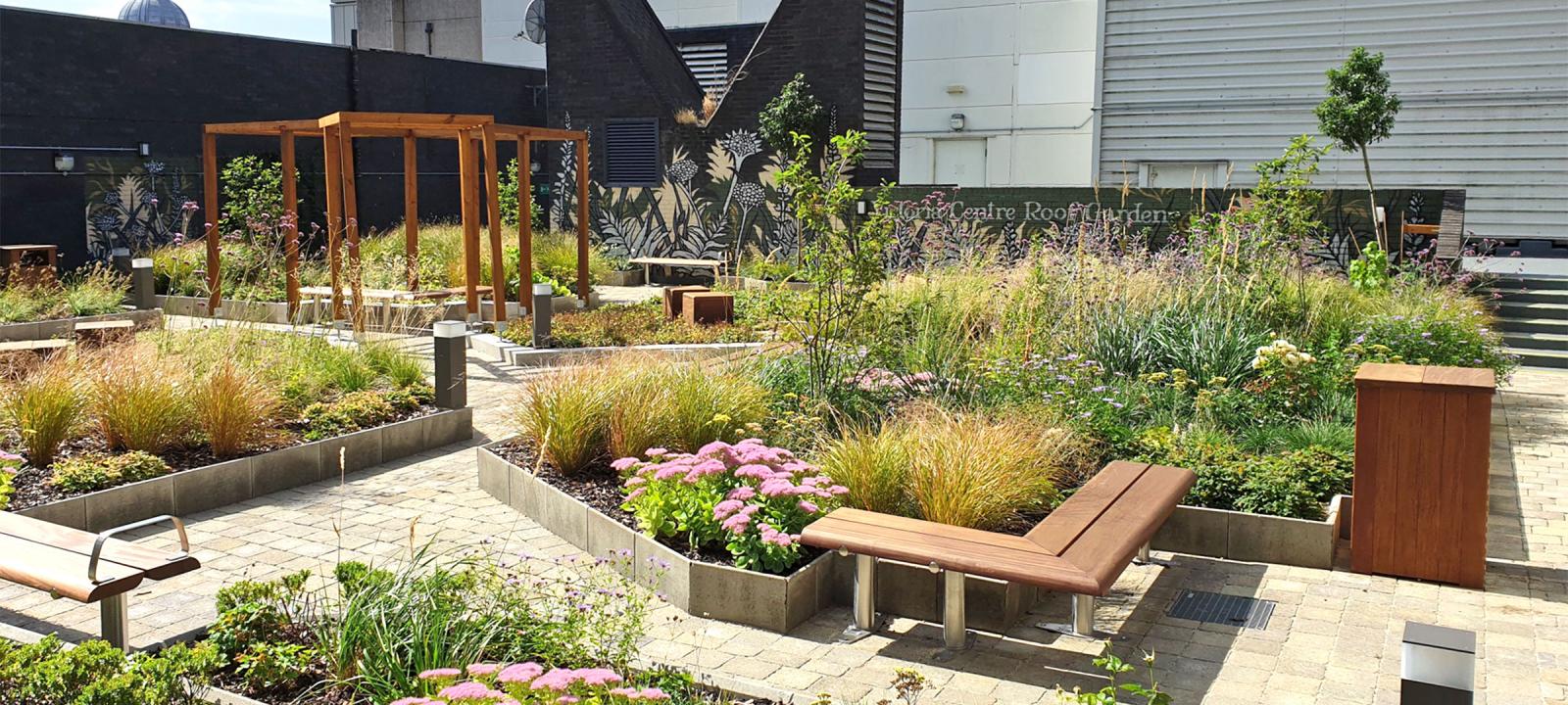 Roof garden with flower beds, walkways, benches and a wooden pergola