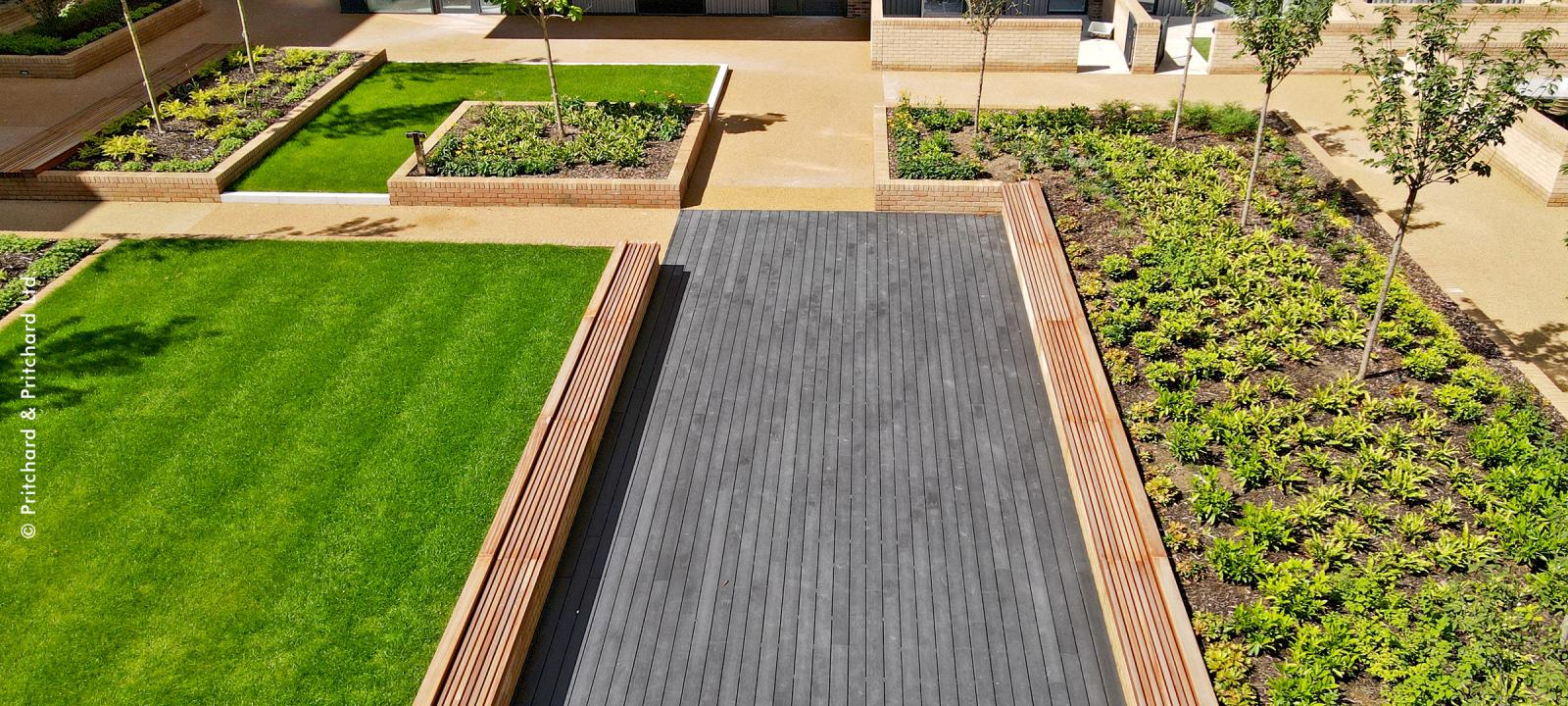 Courtyard with a podium deck, lawn, wooden benches and small trees.