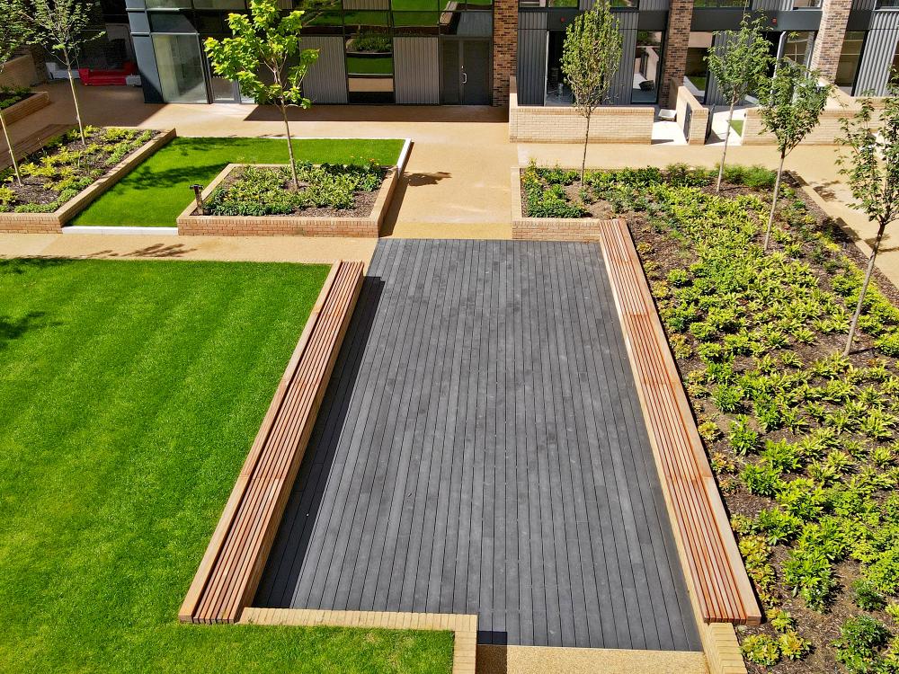 Courtyard with a podium deck, lawn, wooden benches and small trees.