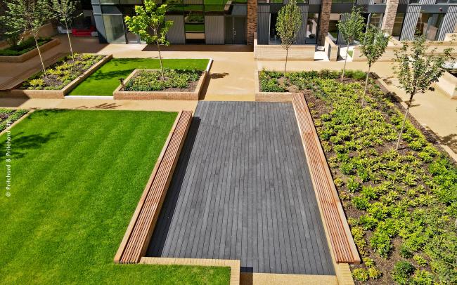 Courtyard with a podium deck, lawn, wooden benches and small trees.